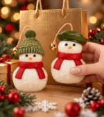 Duas velas de boneco de neve de cachecol vermelho, uma de gorro de tricô verde e outra de boina verde, diante de uma sacola dourada de presente com luzes de Natal ao fundo
