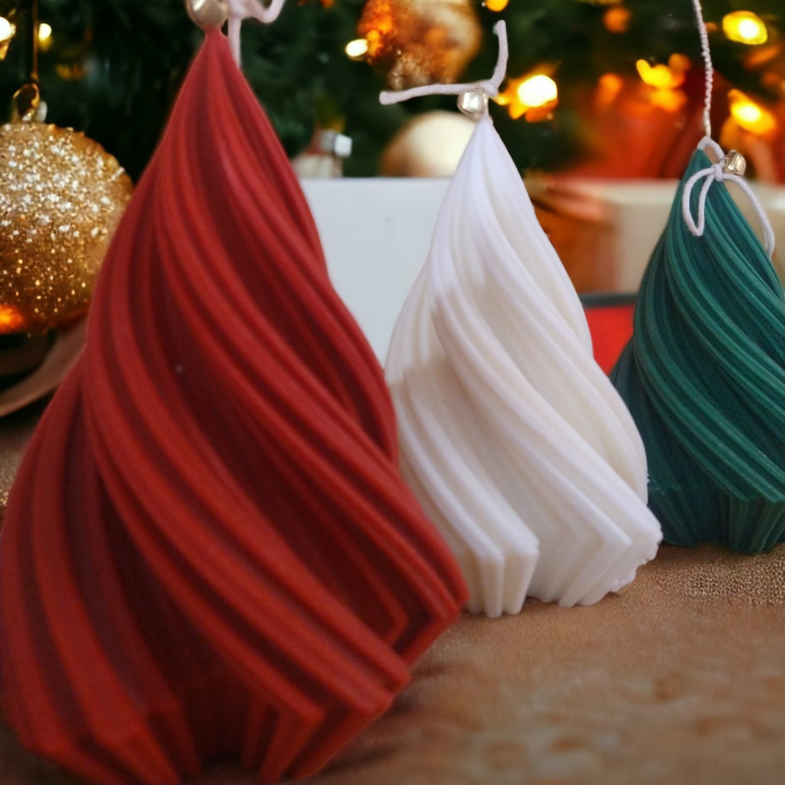 Arvores Torcidas G Três velas em forma de árvore torcida nas cores vermelho, branco e verde, com sininho no pavio, diante de árvore de Natal iluminada